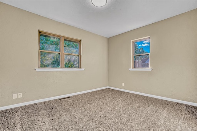 empty room featuring carpet, visible vents, a textured wall, and baseboards