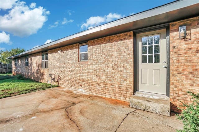 property entrance featuring brick siding, a patio, and a lawn