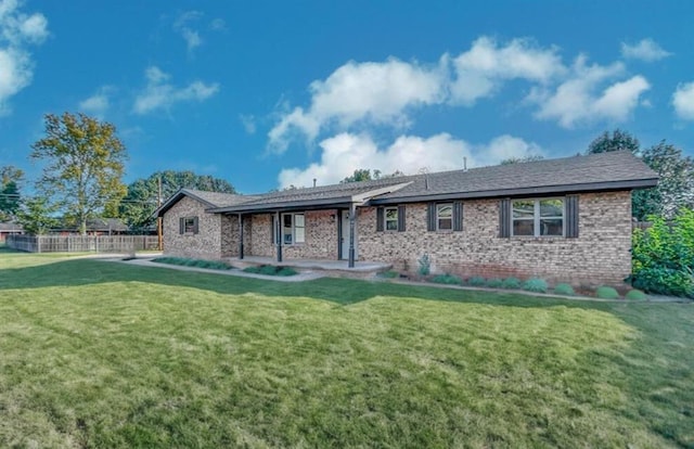 back of house featuring brick siding, a lawn, and fence