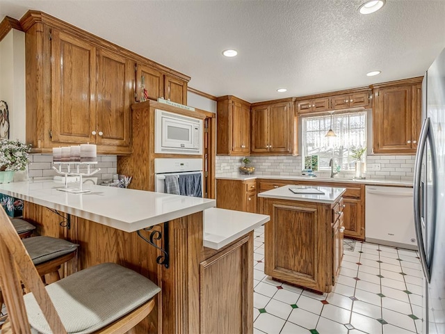 kitchen with a kitchen breakfast bar, kitchen peninsula, a textured ceiling, white appliances, and a kitchen island