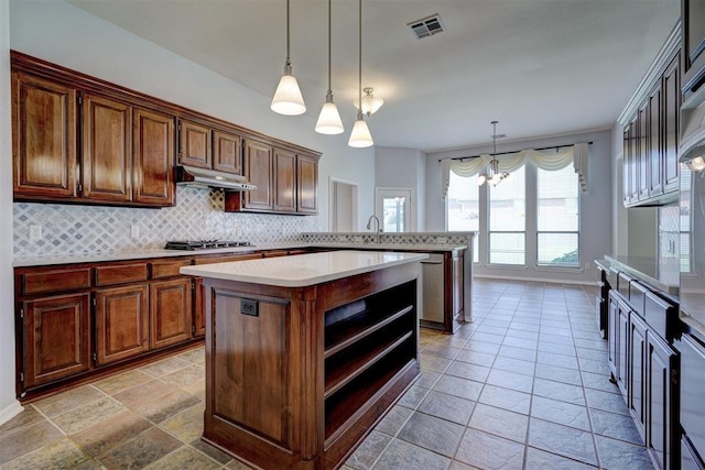 kitchen featuring backsplash, an inviting chandelier, hanging light fixtures, a kitchen island, and stainless steel gas cooktop