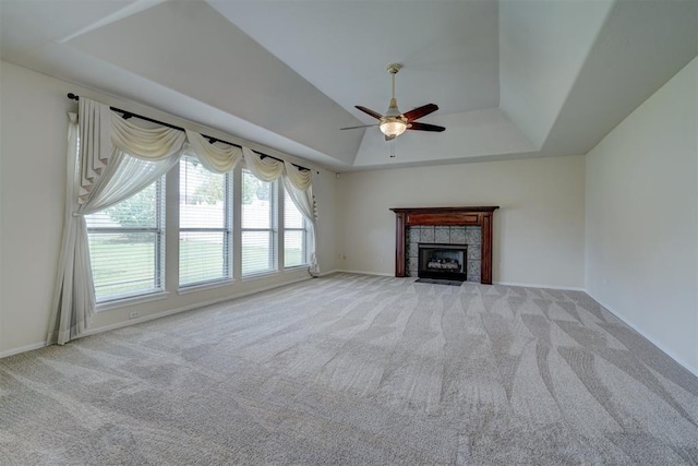 unfurnished living room with ceiling fan, a raised ceiling, light carpet, and a tile fireplace