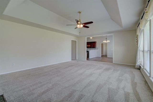 unfurnished living room featuring a tray ceiling, carpet flooring, plenty of natural light, and ceiling fan with notable chandelier