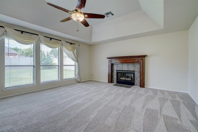 unfurnished living room featuring a raised ceiling, a tile fireplace, ceiling fan, and light colored carpet