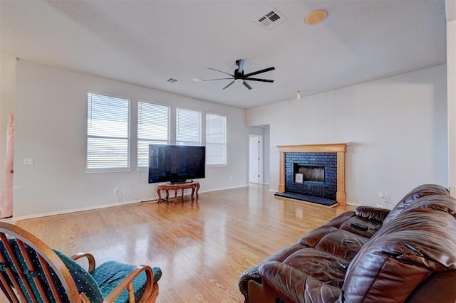 living area with ceiling fan, wood finished floors, visible vents, baseboards, and a brick fireplace