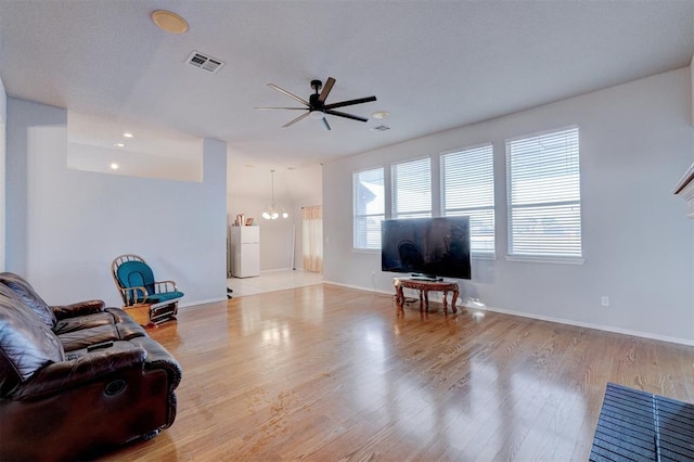 living room with ceiling fan with notable chandelier, wood finished floors, visible vents, and baseboards