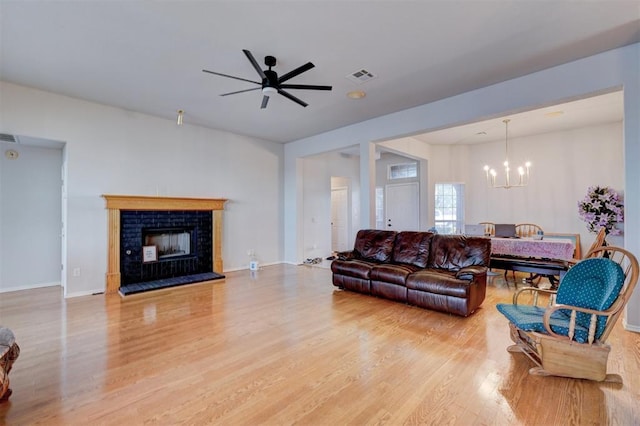 living room featuring light wood finished floors, baseboards, visible vents, a fireplace with raised hearth, and ceiling fan with notable chandelier