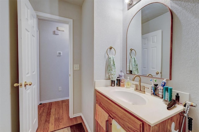 bathroom with a textured wall, wood finished floors, vanity, and baseboards