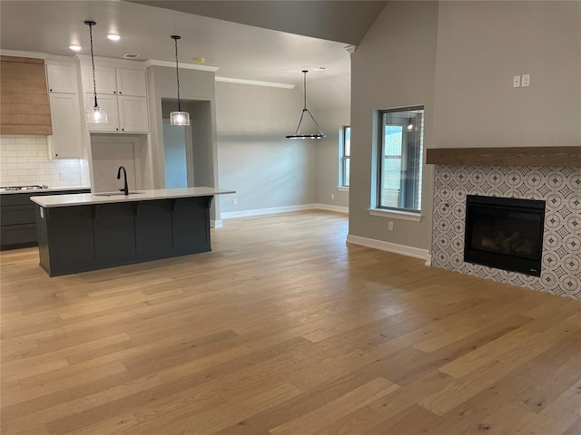 kitchen featuring stainless steel gas cooktop, a center island with sink, white cabinets, light hardwood / wood-style floors, and a tiled fireplace