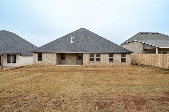 rear view of house featuring a patio area, brick siding, roof with shingles, and fence