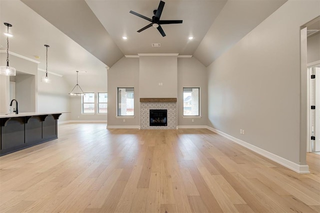 unfurnished living room featuring a tiled fireplace, baseboards, light wood-type flooring, and a ceiling fan