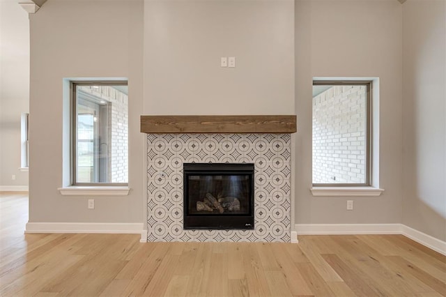 unfurnished living room featuring a wealth of natural light, a fireplace, light wood-type flooring, and baseboards