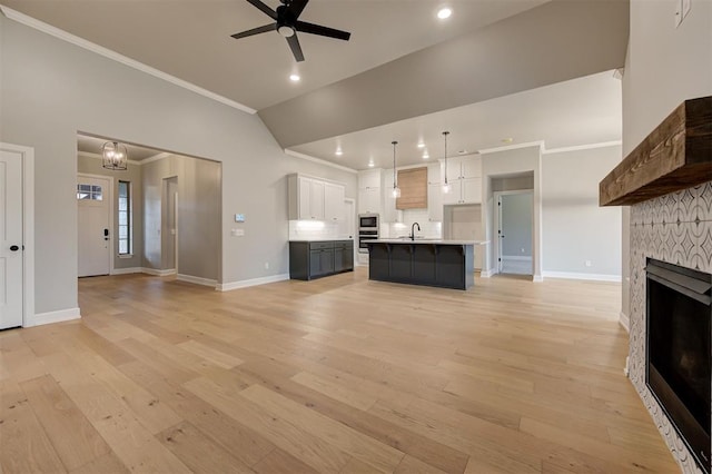 unfurnished living room with light wood finished floors, crown molding, ceiling fan, a stone fireplace, and a sink