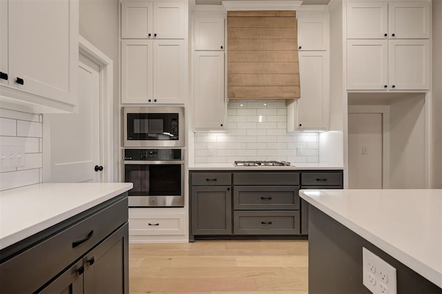 kitchen featuring light wood finished floors, gray cabinetry, light countertops, appliances with stainless steel finishes, and white cabinetry