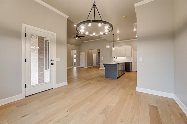 kitchen featuring light wood finished floors, crown molding, decorative light fixtures, open floor plan, and a sink