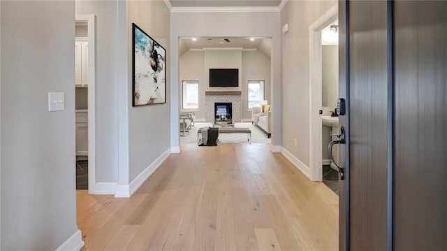 corridor with light wood-type flooring, baseboards, lofted ceiling, and ornamental molding