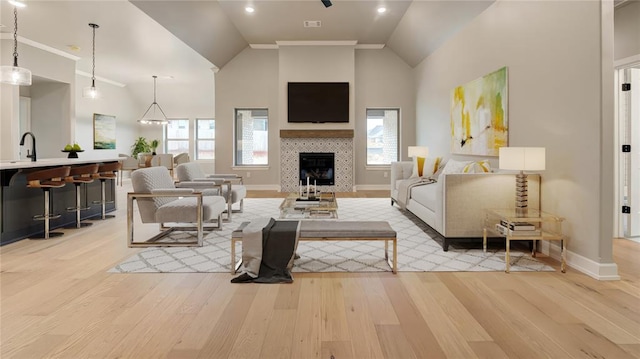 living room featuring baseboards, high vaulted ceiling, a tiled fireplace, and light wood finished floors