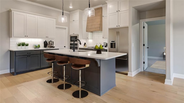 kitchen featuring a kitchen island with sink, a sink, a kitchen breakfast bar, stainless steel appliances, and light countertops