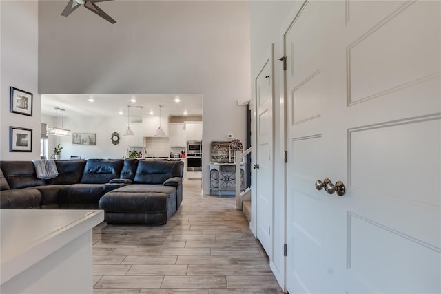 living room with a high ceiling, light hardwood / wood-style flooring, and ceiling fan