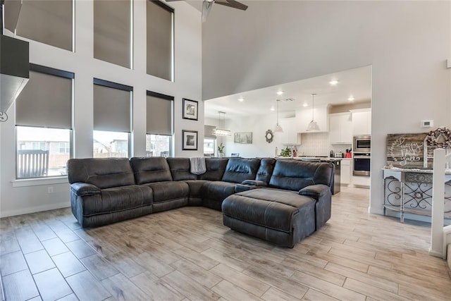 living room with ceiling fan, light hardwood / wood-style floors, and a towering ceiling