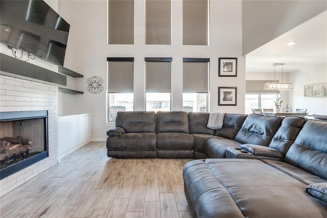 living room featuring light hardwood / wood-style floors, a towering ceiling, and a brick fireplace