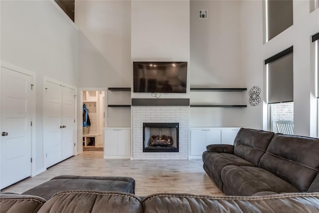 living room with light wood-type flooring, a towering ceiling, and a fireplace