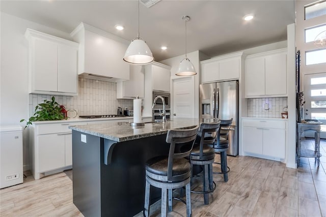 kitchen featuring backsplash, a center island with sink, white cabinets, and stainless steel appliances