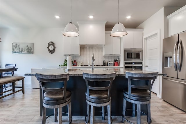 kitchen featuring light stone countertops, white cabinetry, hanging light fixtures, stainless steel appliances, and an island with sink