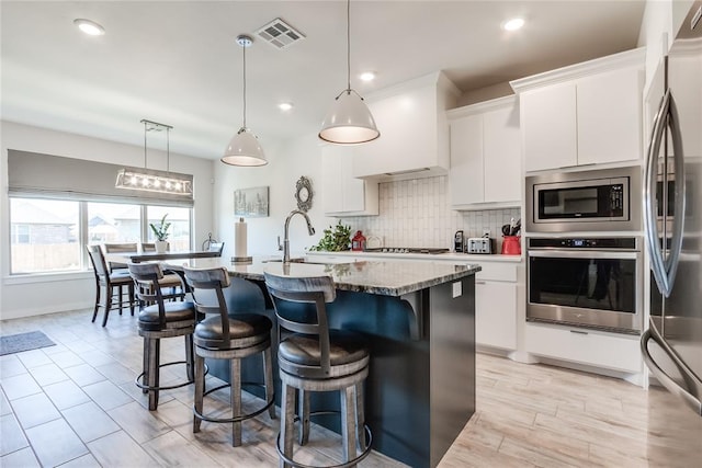 kitchen with sink, hanging light fixtures, a center island with sink, white cabinets, and appliances with stainless steel finishes