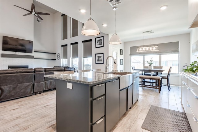 kitchen with ceiling fan, a towering ceiling, pendant lighting, a fireplace, and a center island with sink