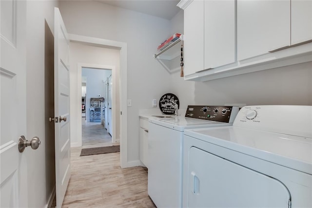 clothes washing area with cabinets, light hardwood / wood-style floors, and washing machine and dryer