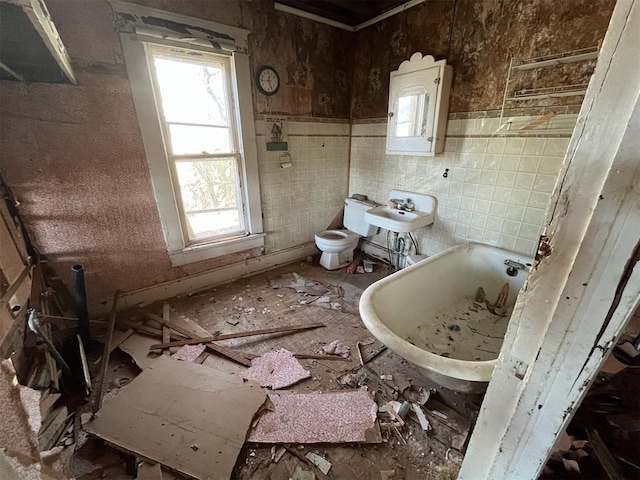 bathroom featuring a bathtub, toilet, sink, and tile walls