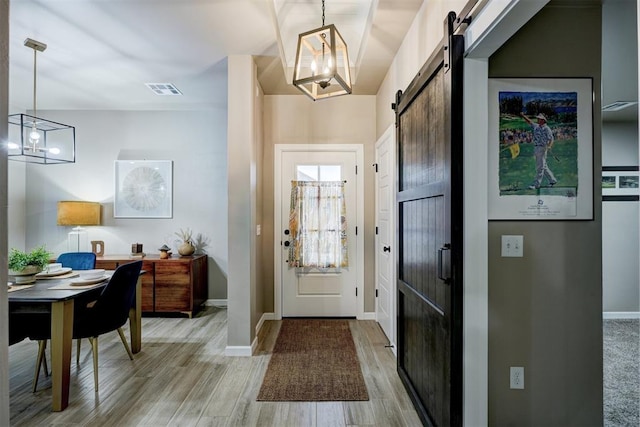 entryway with a barn door, light wood-type flooring, and a notable chandelier