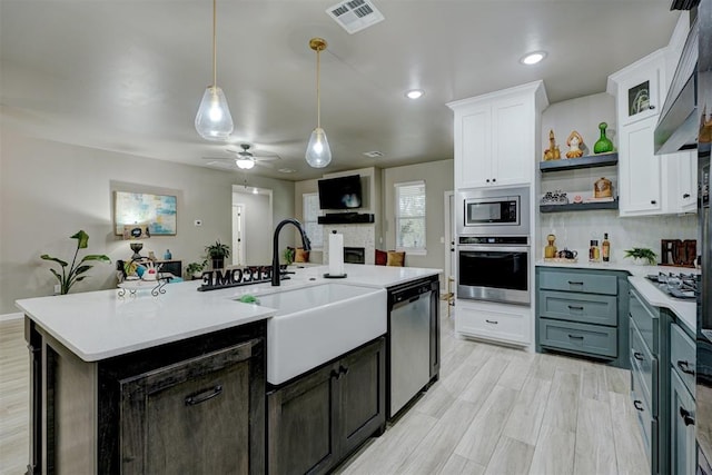 kitchen with a kitchen island with sink, sink, decorative light fixtures, white cabinetry, and stainless steel appliances