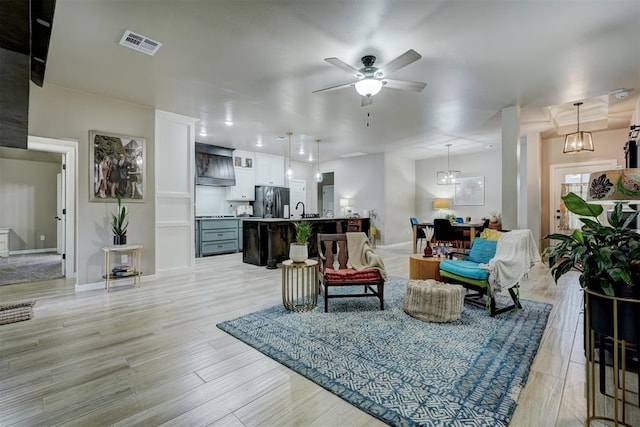 living room with light hardwood / wood-style flooring, ceiling fan with notable chandelier, and sink