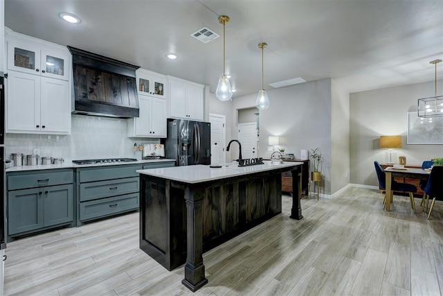 kitchen featuring fridge with ice dispenser, a center island with sink, white cabinets, and pendant lighting