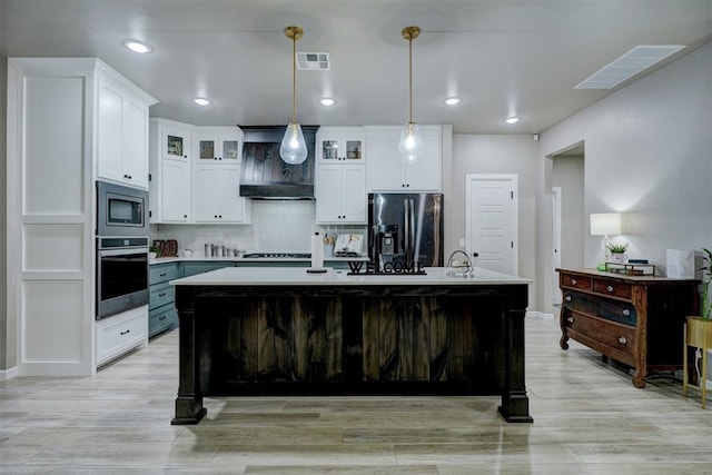 kitchen with a center island with sink, white cabinetry, stainless steel appliances, and hanging light fixtures