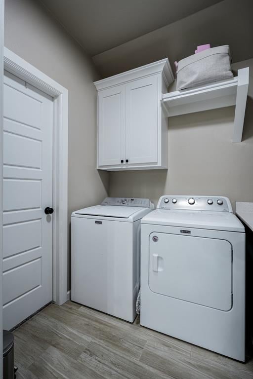 clothes washing area featuring cabinets, light hardwood / wood-style flooring, and washing machine and clothes dryer