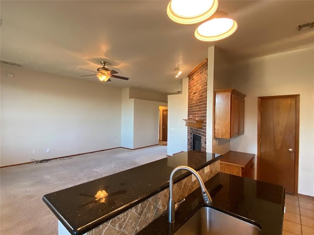 kitchen featuring sink, ceiling fan, light colored carpet, and a fireplace