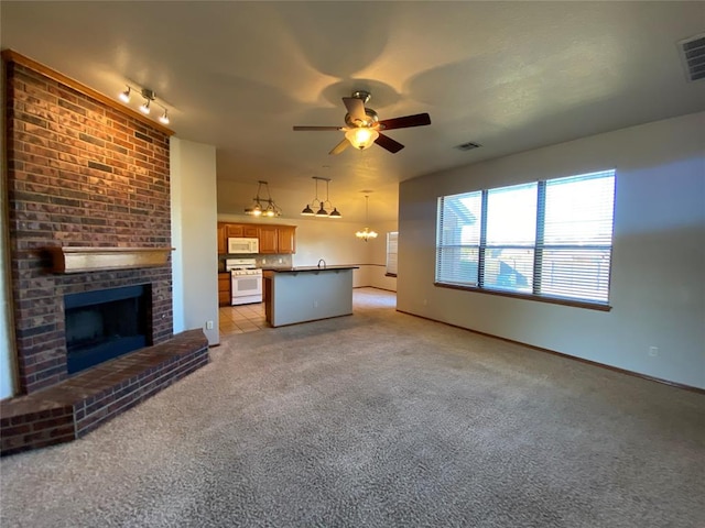 unfurnished living room with a fireplace, light carpet, ceiling fan with notable chandelier, and track lighting