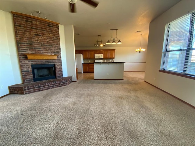 unfurnished living room featuring ceiling fan with notable chandelier, light colored carpet, and a fireplace