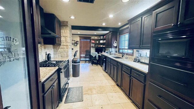 kitchen with light stone countertops, decorative backsplash, wall chimney range hood, black appliances, and sink