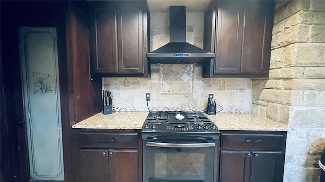 kitchen with gas stove, dark brown cabinetry, light stone countertops, wall chimney range hood, and tasteful backsplash