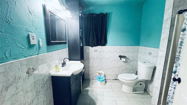 bathroom featuring tile patterned floors, vanity, toilet, and tile walls