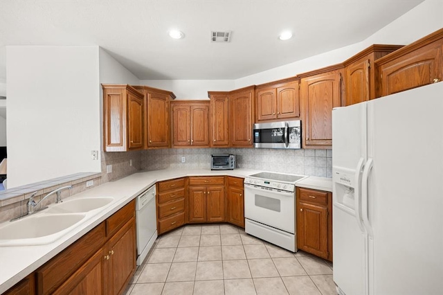 kitchen with white appliances, brown cabinetry, a sink, and tasteful backsplash