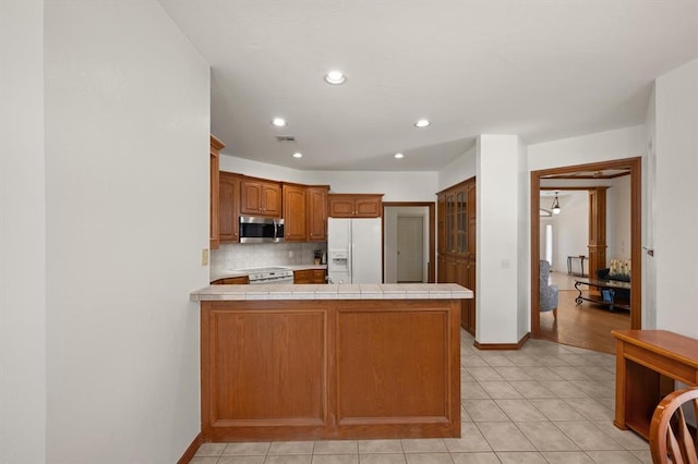 kitchen with tile countertops, a peninsula, electric stove, white fridge with ice dispenser, and stainless steel microwave