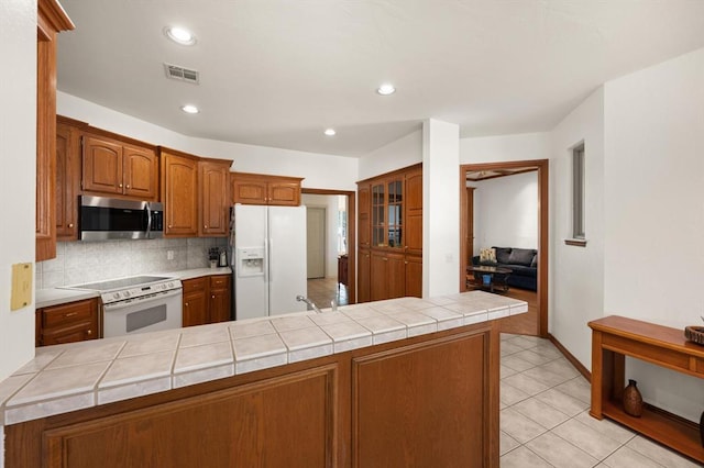 kitchen featuring tasteful backsplash, visible vents, brown cabinetry, white appliances, and a peninsula