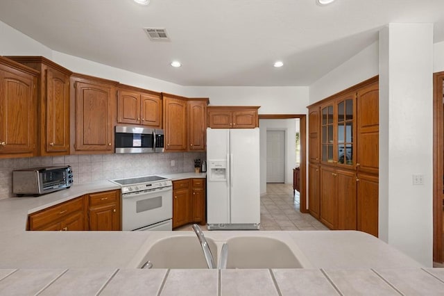 kitchen featuring a toaster, white appliances, visible vents, decorative backsplash, and brown cabinetry