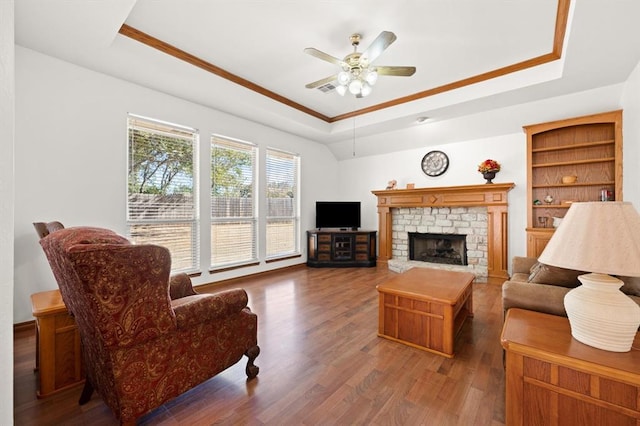 living area with ceiling fan, wood finished floors, visible vents, a brick fireplace, and a tray ceiling