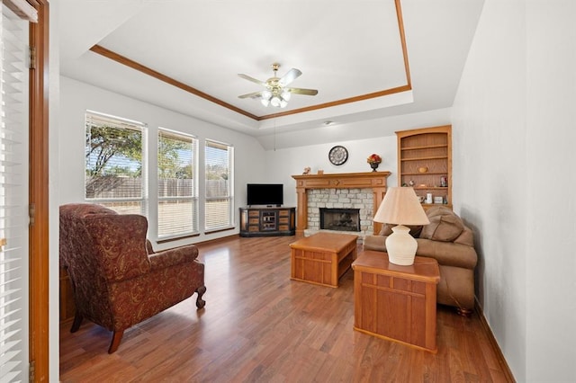 living area with a tray ceiling, a fireplace, ornamental molding, ceiling fan, and wood finished floors